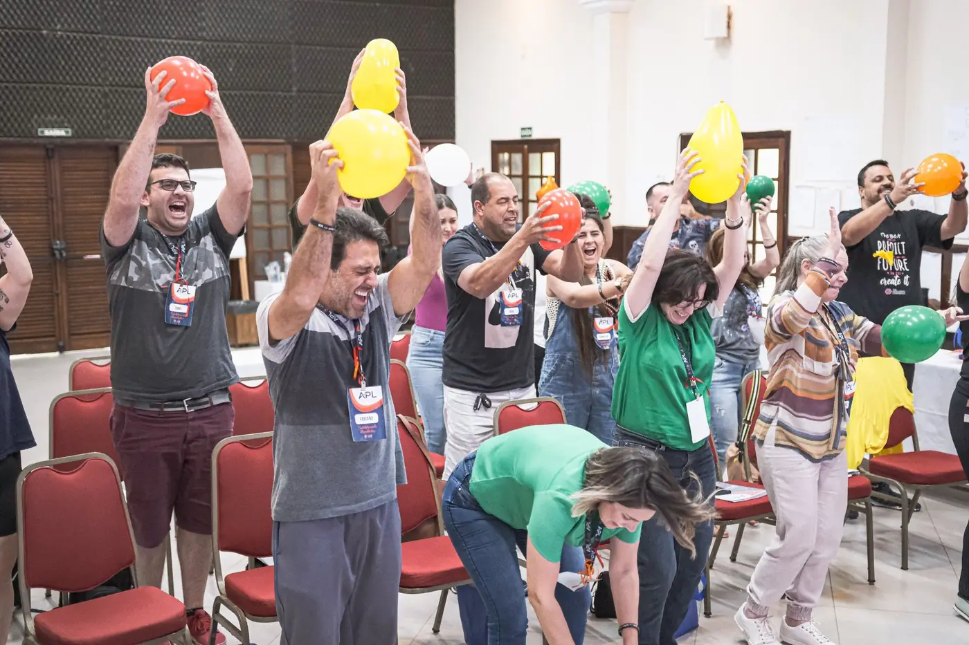Participantes de pé erguendo balões coloridos e rindo durante uma dinâmica