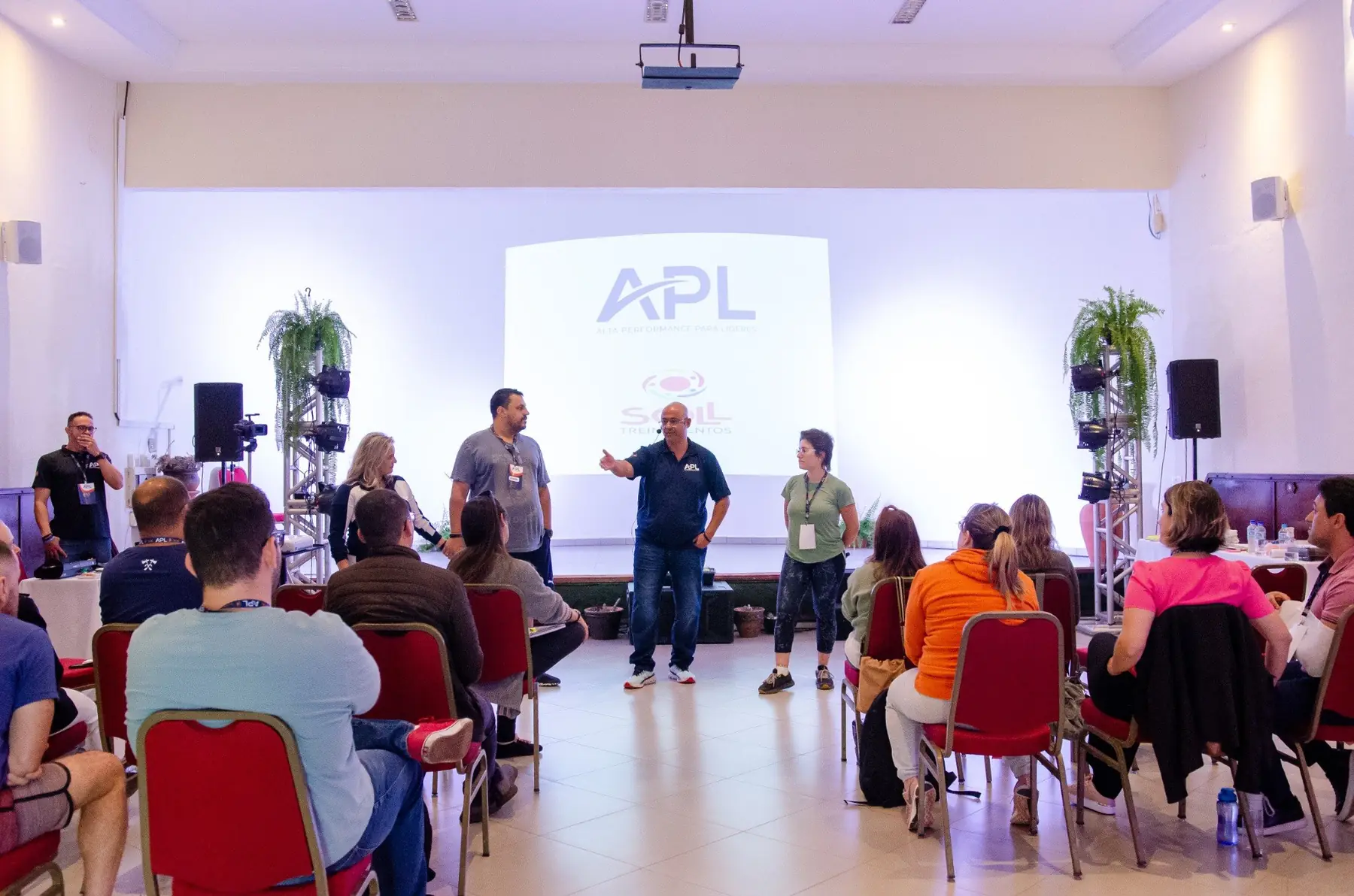 Sóstenes conduzindo uma turma do APL diante do telão com o logo do programa