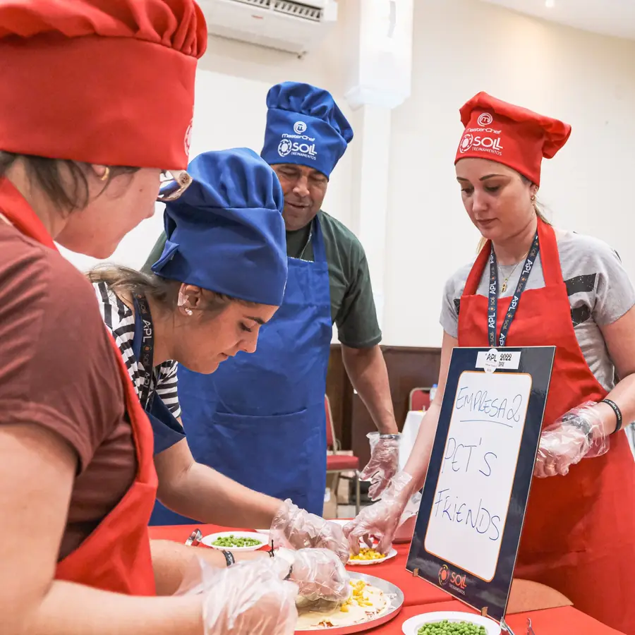 Equipes com chapéus de cozinheiro montando um prato em uma dinâmica de cozinha