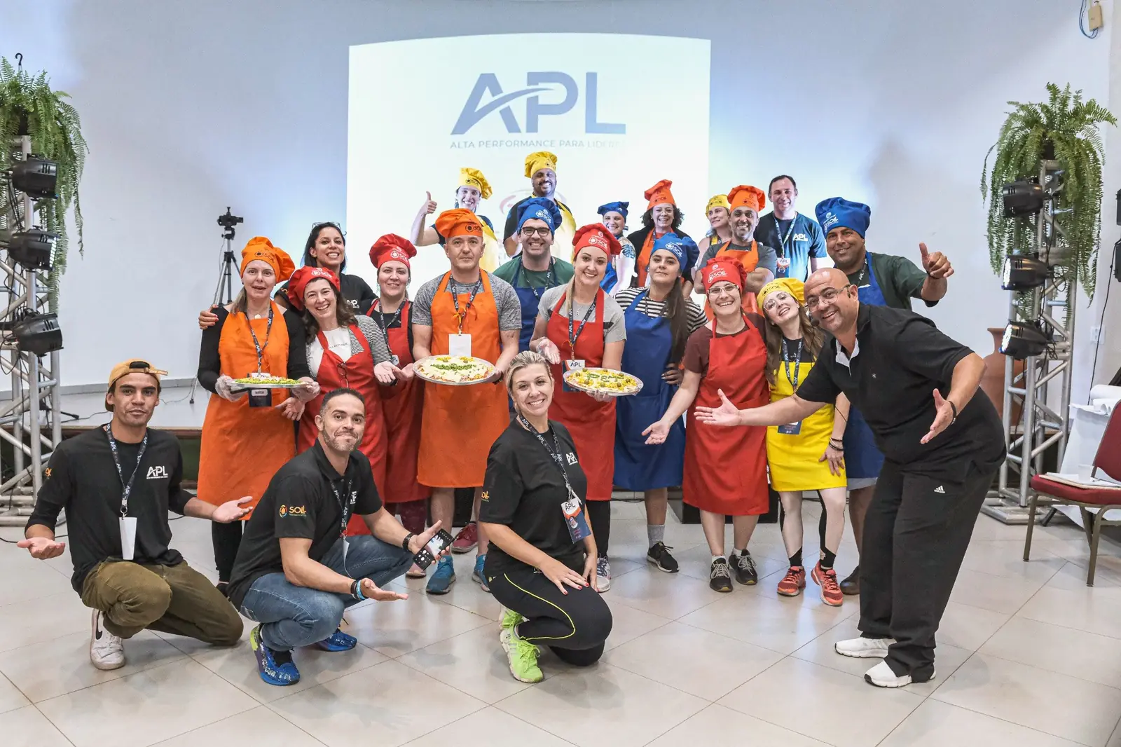 Turma do APL reunida com aventais coloridos, segurando os pratos preparados na dinâmica